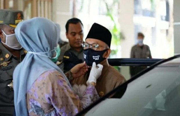 Foto: Bunda Fitri Rapikan Masker Bupati Busyro. (Foto Facebook Nurfitriana Busyro)
