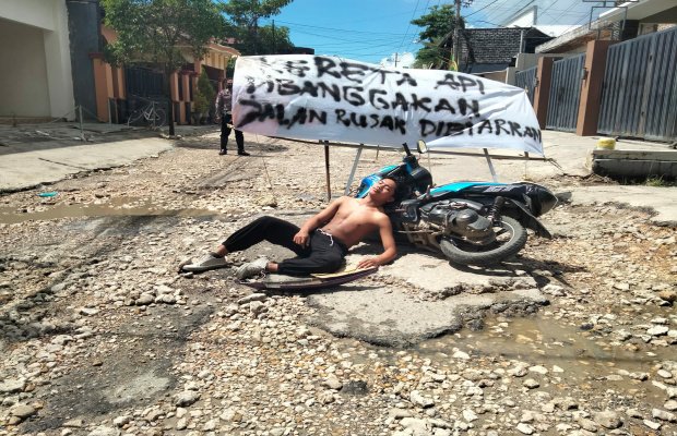 Foto: Seorang aktivis dengan benner bertuliskan "Kereta Api Dibanggakan, Jalan Rusak Dibiarkan" saat melakukan aksi