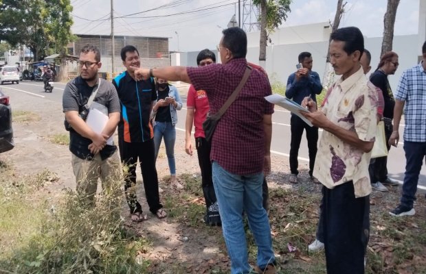 Foto : Puji (bercelana jeans, mengenakan tas pundak, menunjuk ke lokasi kavling dengan tangan kiri).