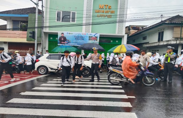 Foto: Kasat Lantas Polres Batu, AKP Kevin Ibrahim saat menyebrangkan pelajar di jalan raya