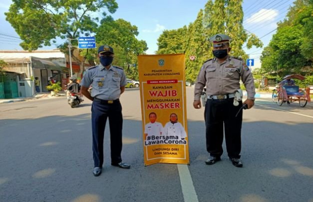 Foto: Dua petugas gabungan tengah membentangkan banner bertuliskan wajib menggunakan masker