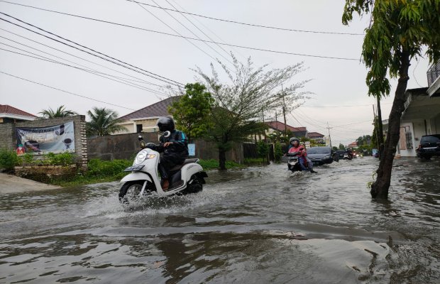 Foto: Pengendara saat melintas ditengah genangan air hujan